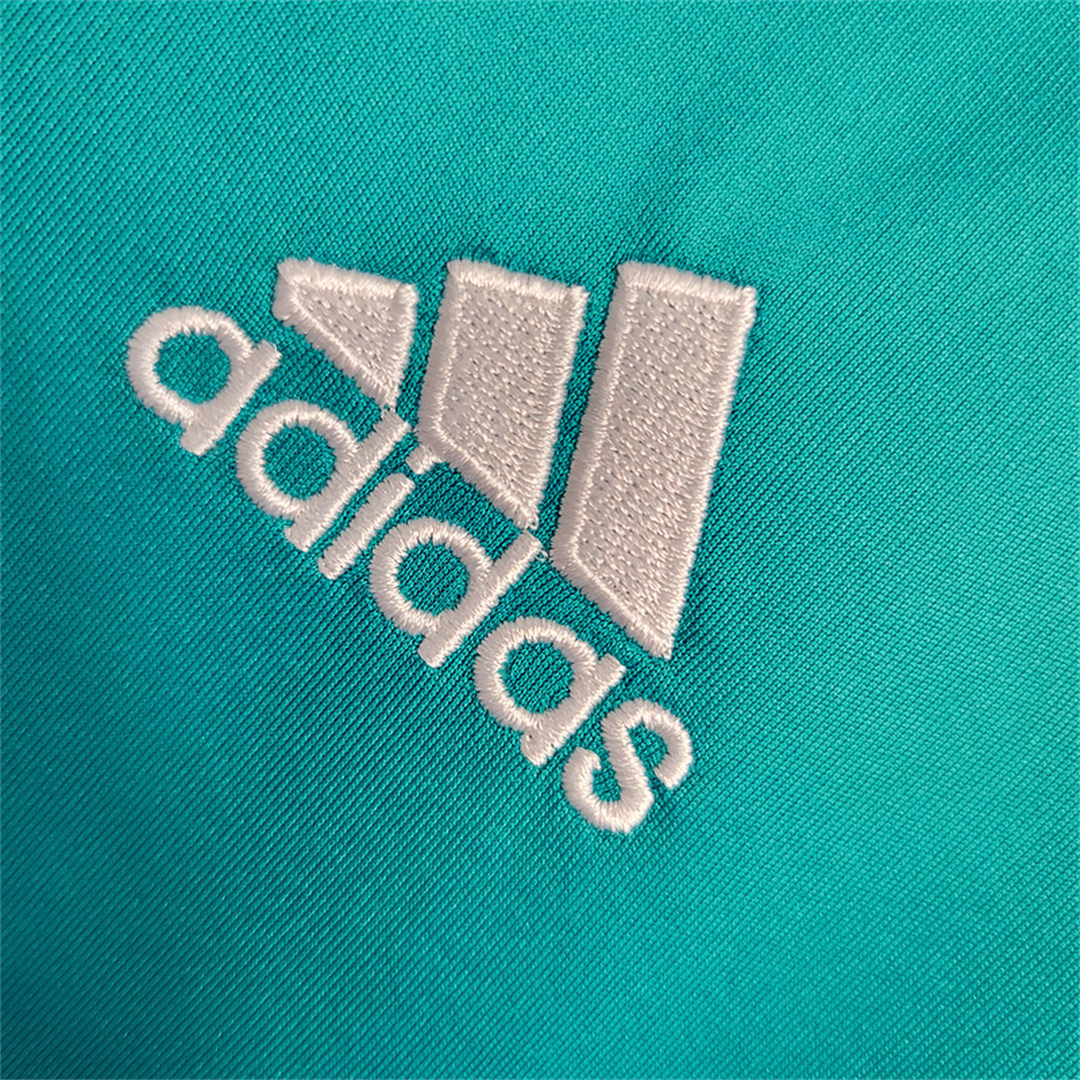 Dettaglio ravvicinato dello stemma del Adidas ricamato in bianco su tessuto turchese.
