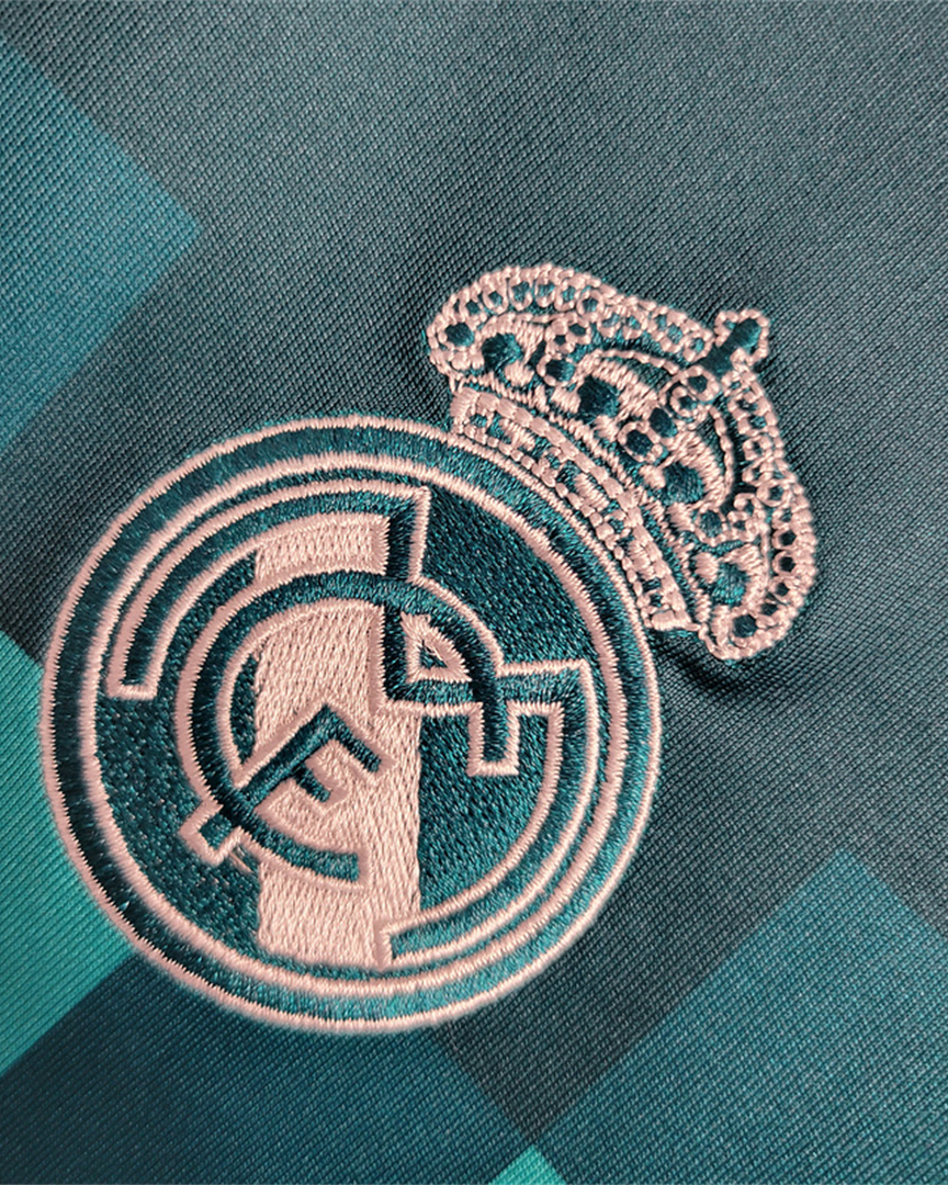 Dettaglio ravvicinato dello stemma del club Real Madrid ricamato in bianco su tessuto turchese.