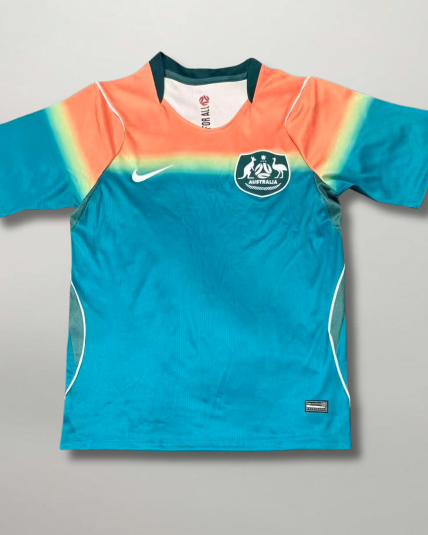 Fronte della maglia away dell'Australia 2026 turchese con spalle sfumate oro e arancione e stemma sul petto