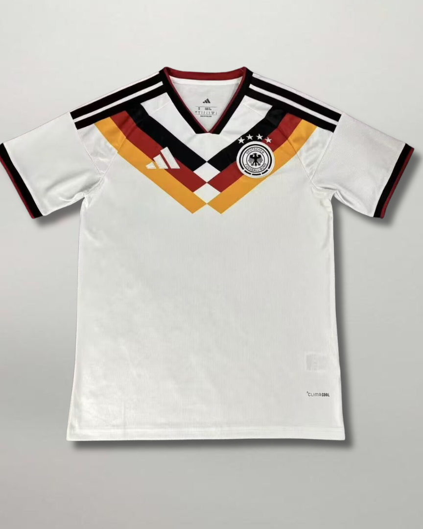 Fronte della maglia home della Germania 2026 bianca con motivo geometrico nero rosso oro sul petto e stemma centrale