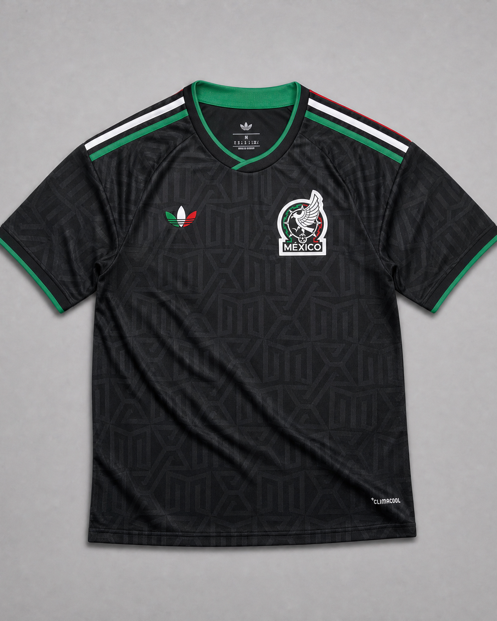 Maglia third Messico Coppa del Mondo 2026 — vista frontale su superficie in legno, colore nero con pattern geometrico azteco tono su tono, colletto rotondo con bordino tricolore verde-bianco-rosso e stemma nazionale sul petto sinistro