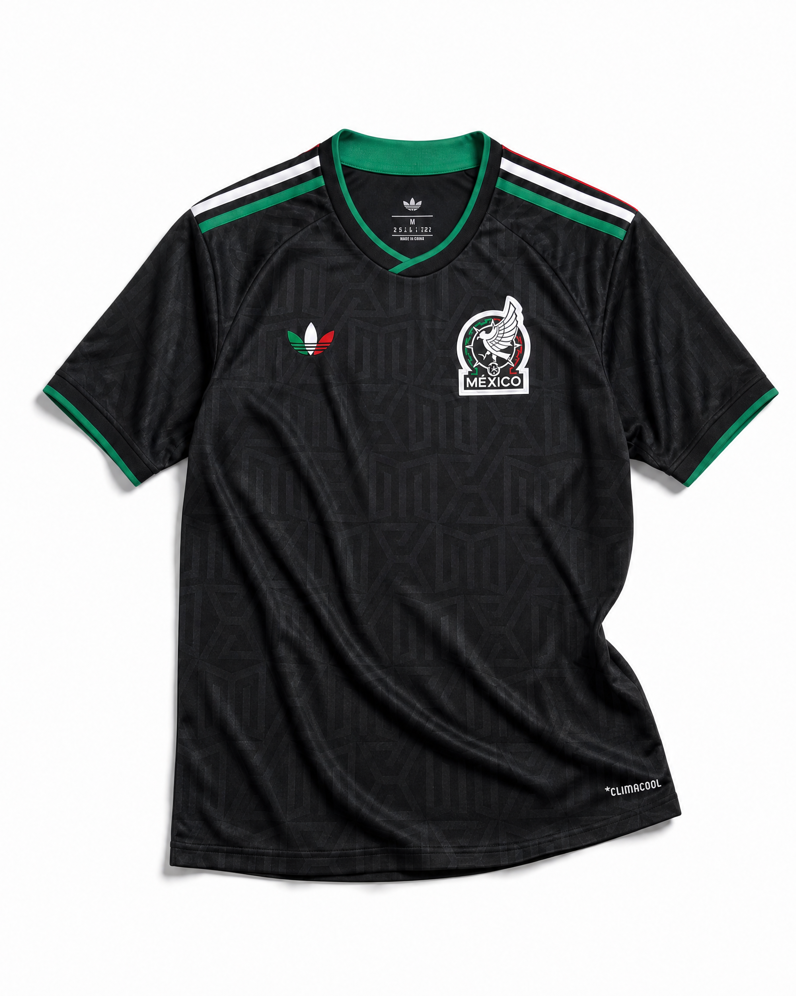 Maglia third Messico Coppa del Mondo 2026 — vista frontale su superficie in legno, colore nero con pattern geometrico azteco tono su tono, colletto rotondo con bordino tricolore verde-bianco-rosso e stemma nazionale sul petto sinistro