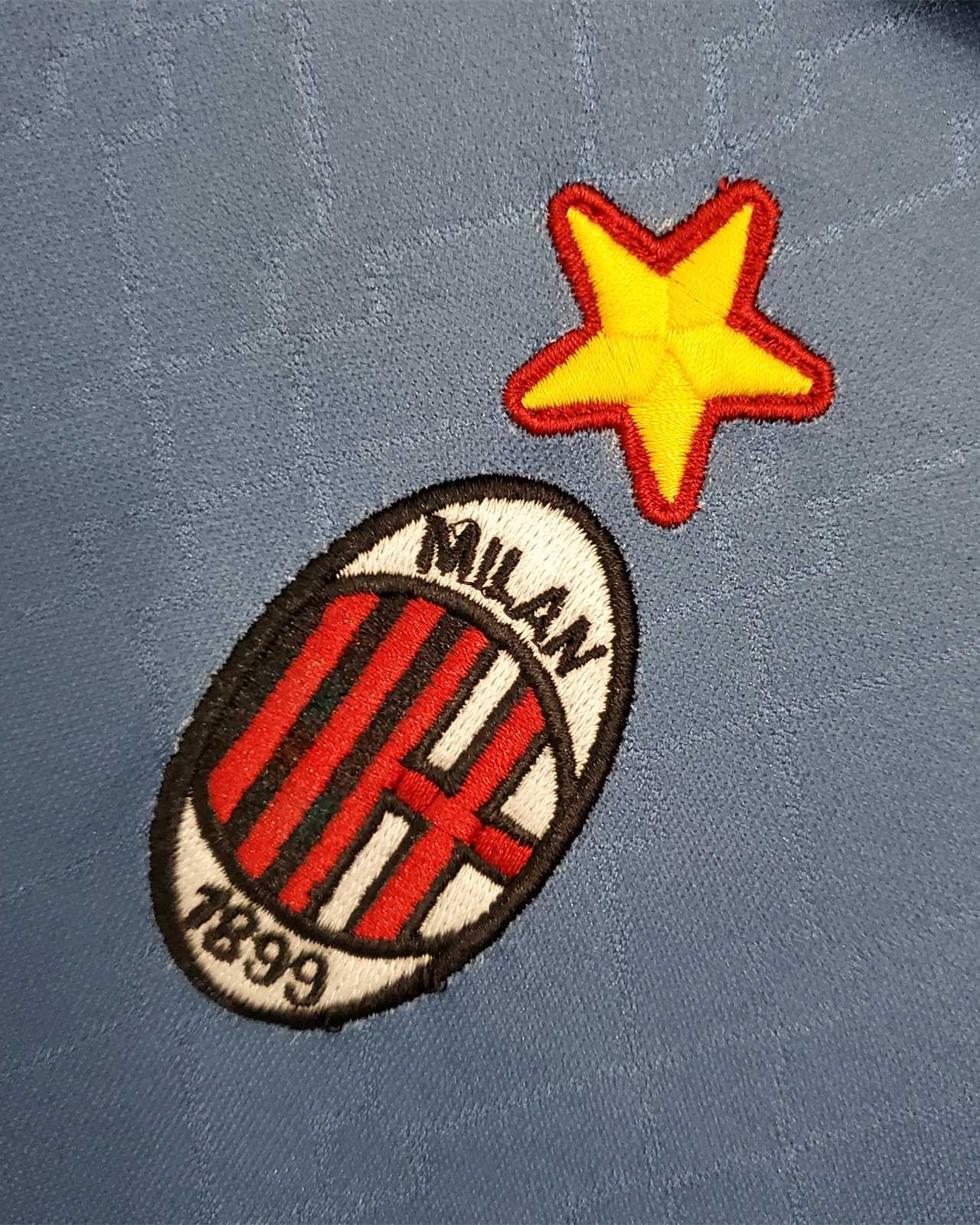 Primo piano dello stemma del Milan con stella ricamata su maglia blu 1995/96.