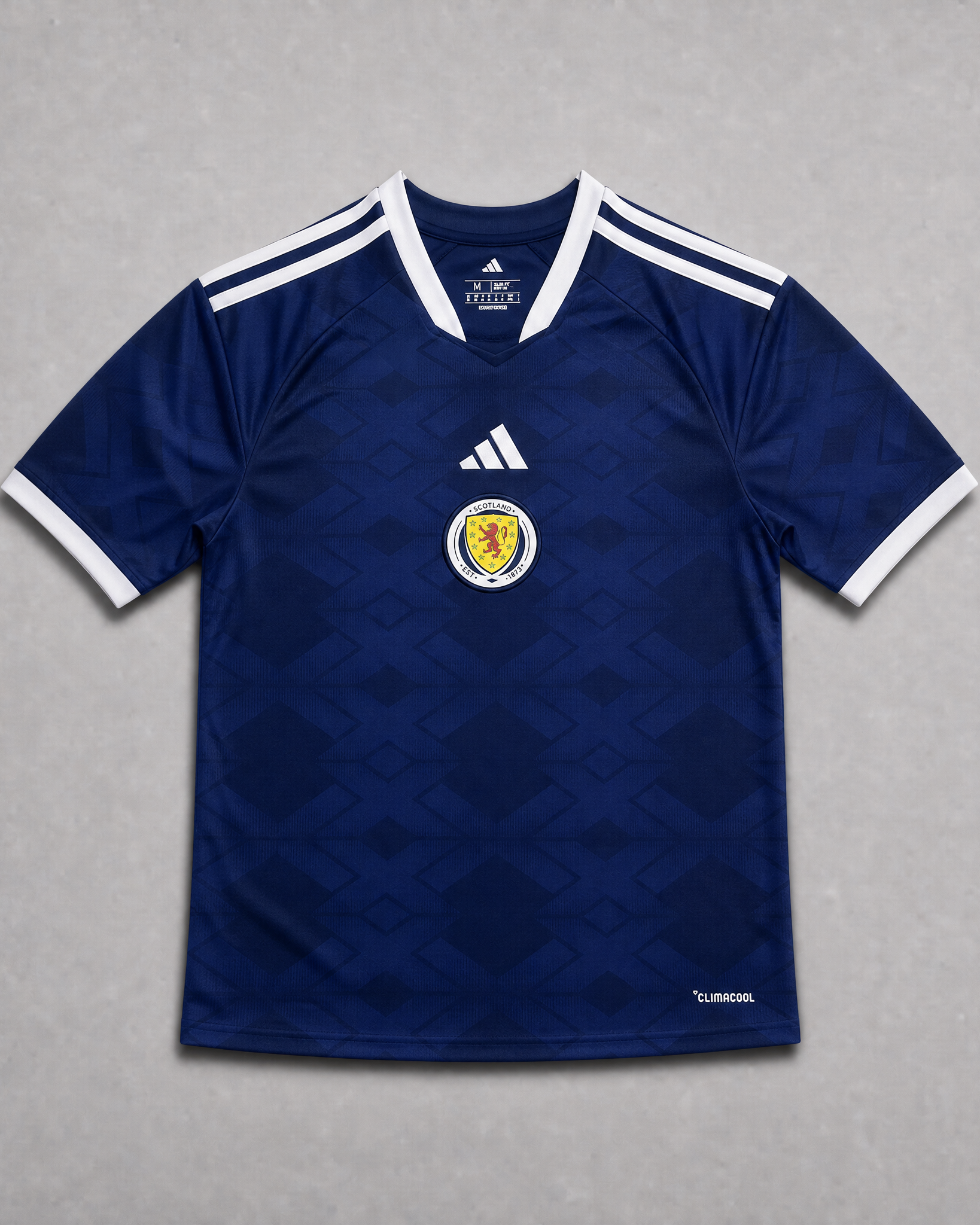 Maglia home Scozia Coppa del Mondo 2026 — vista frontale su superficie grigia, tessuto blu navy con colletto a V con bordino bianco, stemma della federazione scozzese sul petto sinistro, maniche con profili bianchi