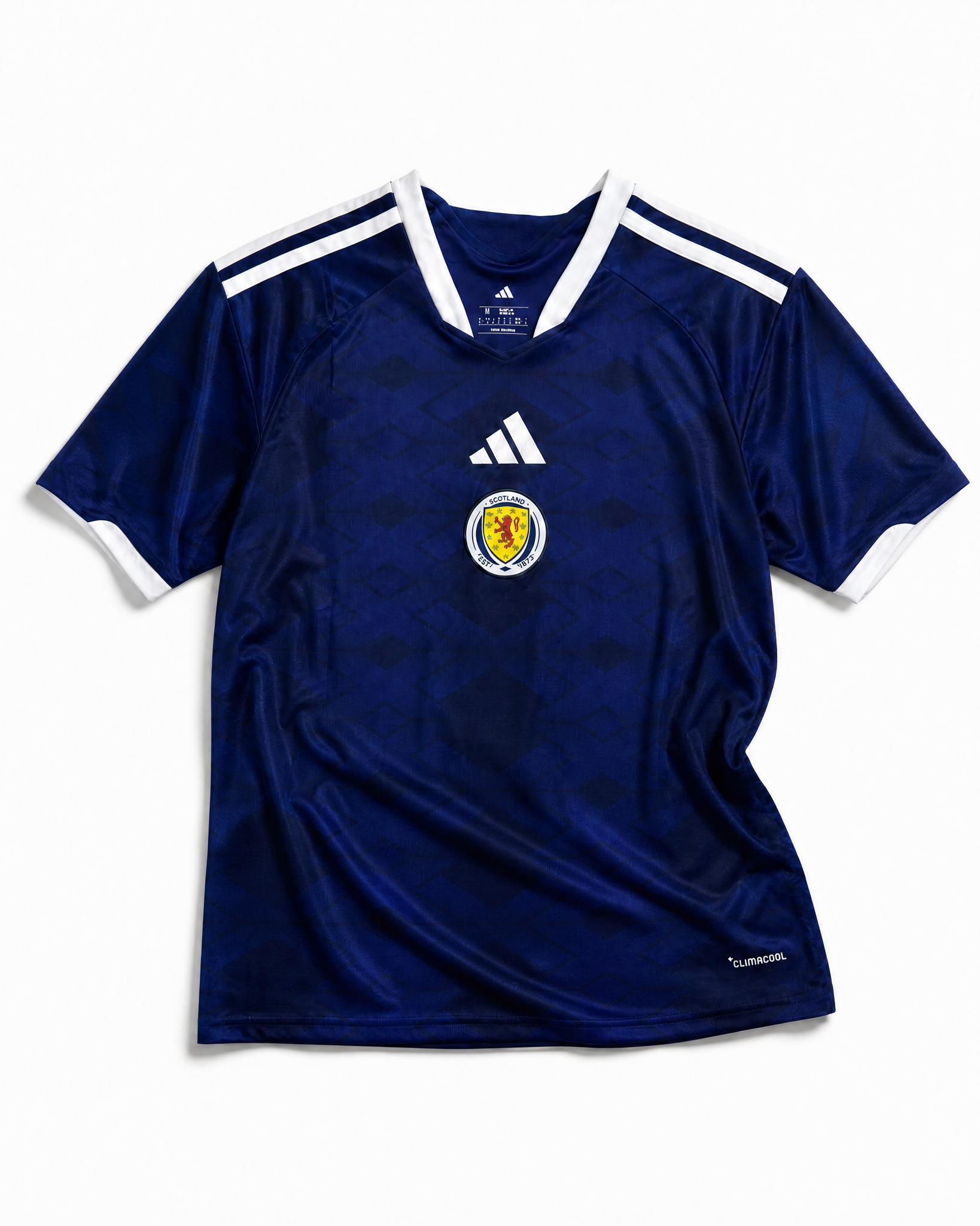 Maglia home Scozia Coppa del Mondo 2026 — vista frontale su superficie grigia, tessuto blu navy con colletto a V con bordino bianco, stemma della federazione scozzese sul petto sinistro, maniche con profili bianchi