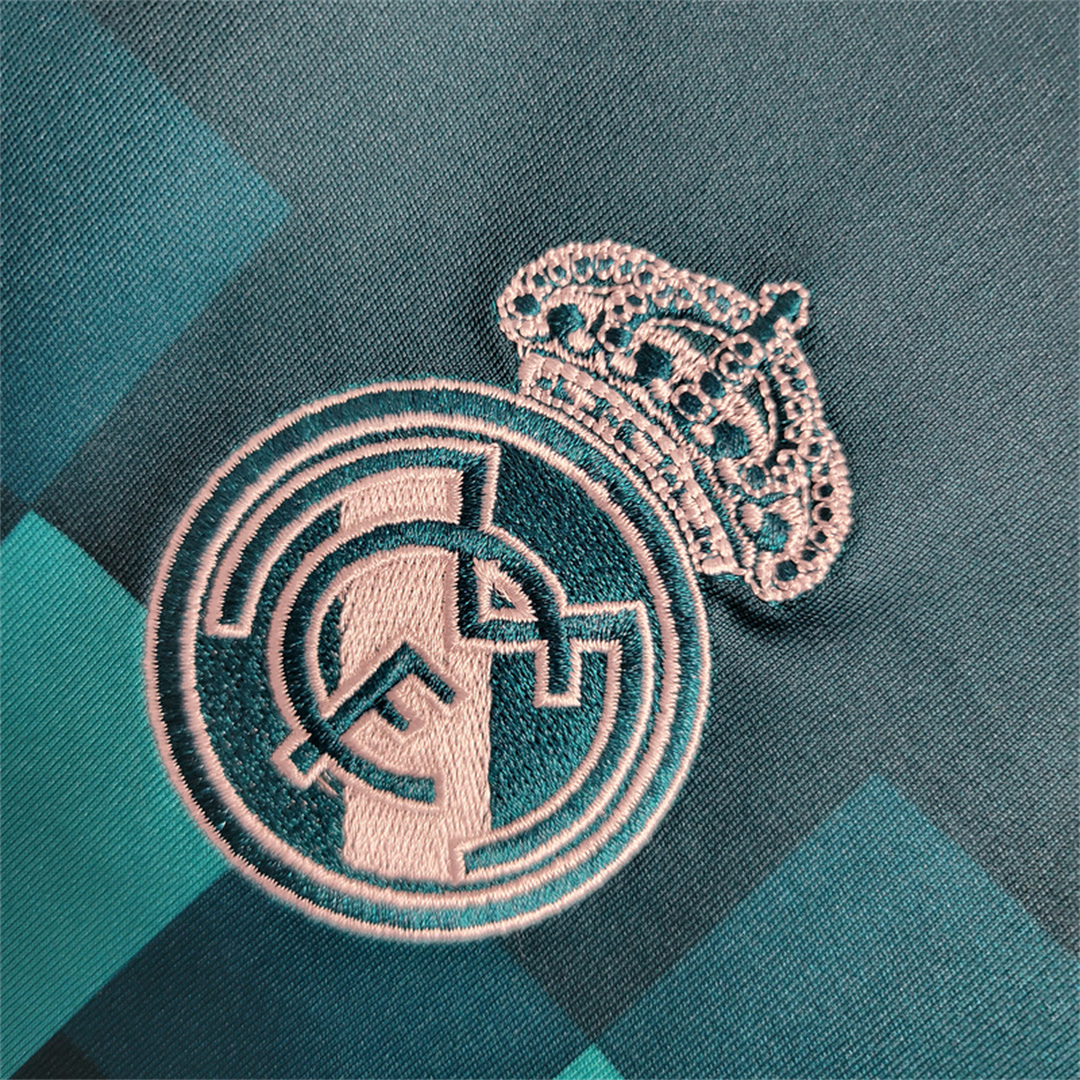 Dettaglio ravvicinato dello stemma del club Real Madrid ricamato in bianco su tessuto turchese.