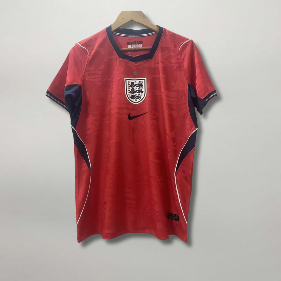 Fronte della maglia away dell'Inghilterra 2026 scura con dettagli geometrici colorati sui fianchi e stemma ricamato