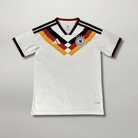 Fronte della maglia home della Germania 2026 bianca con motivo geometrico nero rosso oro sul petto e stemma centrale
