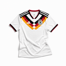 Fronte della maglia home della Germania 2026 bianca con motivo geometrico nero rosso oro sul petto e stemma centrale
