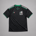 Maglia third Messico Coppa del Mondo 2026 — vista frontale su superficie in legno, colore nero con pattern geometrico azteco tono su tono, colletto rotondo con bordino tricolore verde-bianco-rosso e stemma nazionale sul petto sinistro
