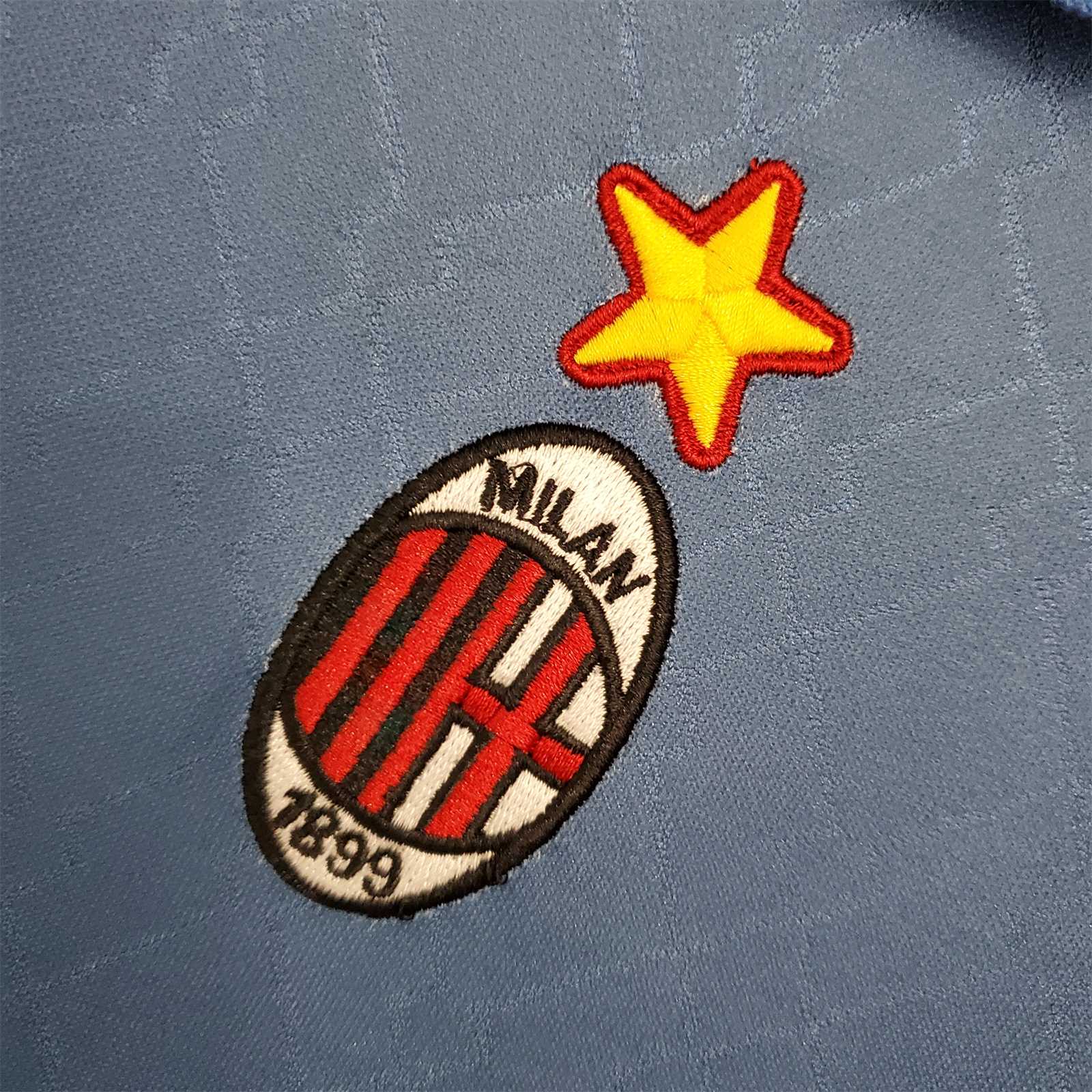 Primo piano dello stemma del Milan con stella ricamata su maglia blu 1995/96.