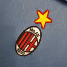 Primo piano dello stemma del Milan con stella ricamata su maglia blu 1995/96.
