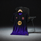 Maglia away Barcellona 2026/27 nero e viola su gruccia in legno, vista frontale